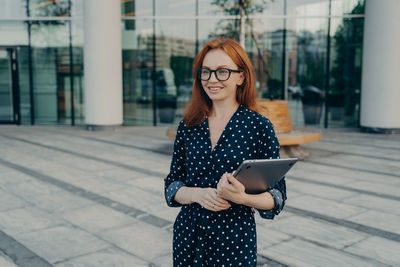 Portrait of young woman wearing sunglasses while standing in city