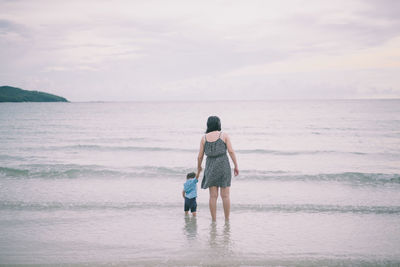 Rear view of woman standing on beach against sky