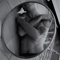 Midsection of shirtless man with tattoo reflecting in mirror