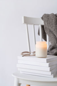 Candle mockup design. cozy interior with white chair, warm plaid, books and autumn leaves