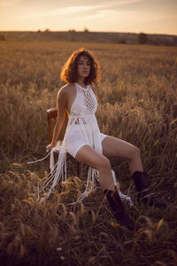  portrait of a curly-haired woman in white clothes dress sit on a field with dry grass in autumn