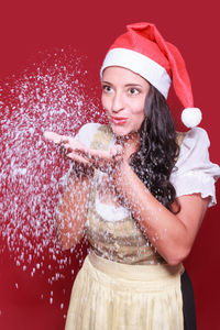 Smiling woman blowing snow against red background