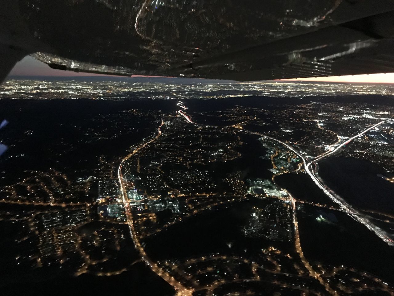 HIGH ANGLE VIEW OF ILLUMINATED CITYSCAPE BY SEA AGAINST SKY