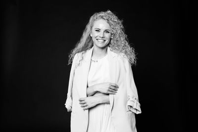 Portrait of smiling woman with curly hair standing against black background