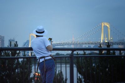 Rear view of man looking at suspension bridge against sky