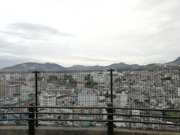 Fence by buildings against sky in city