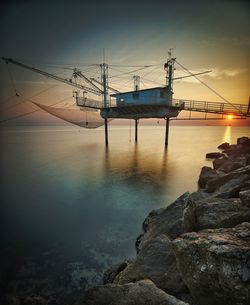 Fishing net in sea against sky during sunset