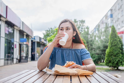 Hungry stylish woman, enjoying eating a burger outdoors, dressed in jeans shirt, wearing sunglasses