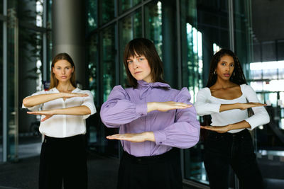 Portrait of women gesturing equal sign while standing against building