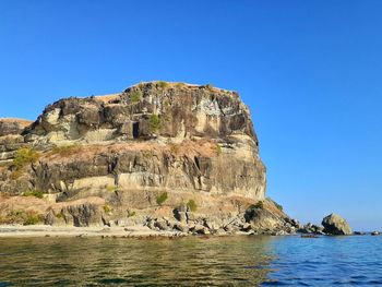 Rock formation by sea against clear blue sky