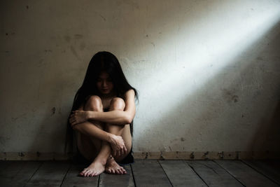 Full length of depressed woman sitting against wall