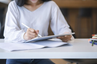 Midsection of woman holding paper while sitting on table