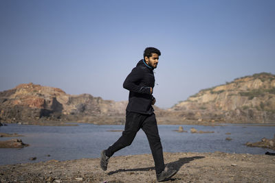 Young indian fit boy jogging in the morning near a lake situation in middle of a mountain area.