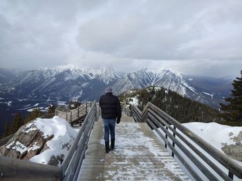 Rear view of man walking on boardwalk against snowcapped mountains