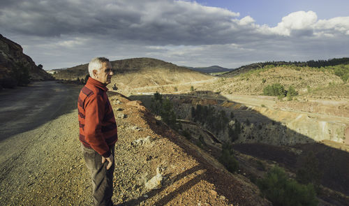 Senior man standing by mountain against cloudy sky