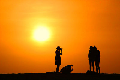 Silhouette people against orange sky during sunset