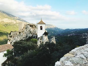 Historic bell tower by mountains against sky