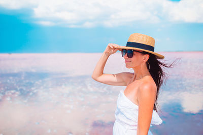 Woman wearing hat standing by sea against sky