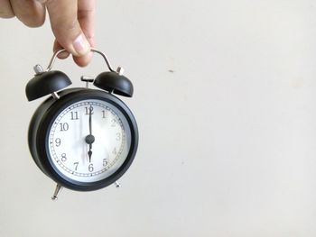 Cropped hand of person holding alarm clock against white background