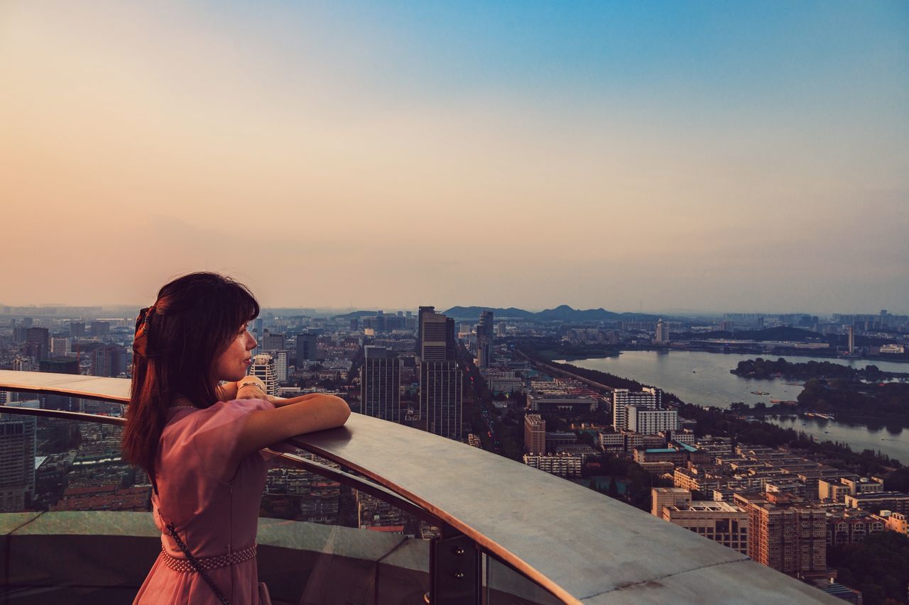 building exterior, architecture, built structure, cityscape, sky, city, one person, standing, sunset, real people, lifestyles, leisure activity, nature, women, adult, rear view, waist up, crowded, building, outdoors, looking at view, hairstyle