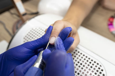 The manicurist cuts the cuticles of the nails with an electric milling machine wearing blue latex