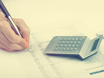 Cropped image of hand holding paper against white wall
