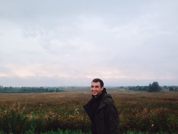 Portrait of young man standing on grassy field against sky