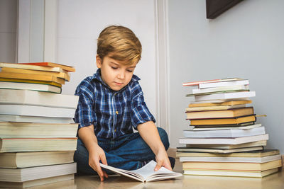 Full length of boy reading book while sitting on hardwood floor at home