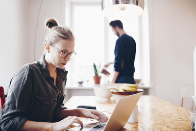 Woman working on laptop against man watering plant at home