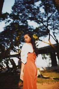 Low angle view portrait of woman standing against trees