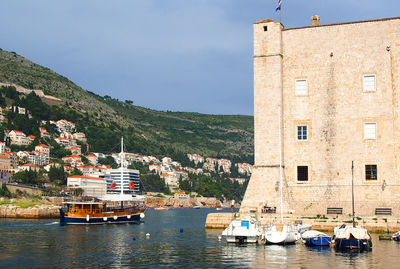 Boats moored on sea by mountain against sky