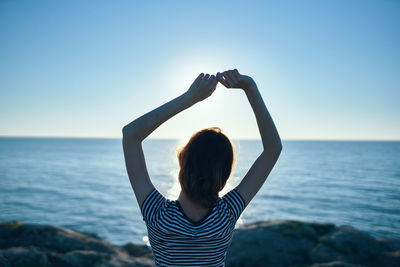 Rear view of woman standing with arms raised against clear sky