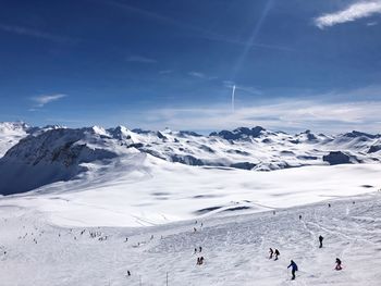 People skiing on landscape against sky during winter