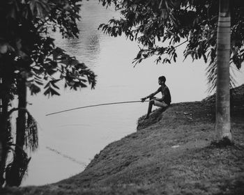 Side view of man fishing in lake by trees on field