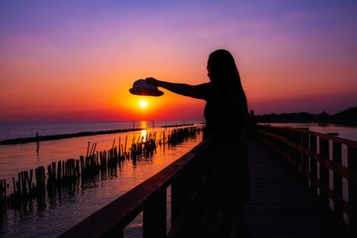 Silhouette woman standing by railing against sea during sunset