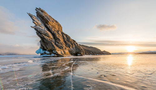 Scenic view of rock formation in frozen sea against sky at sunset