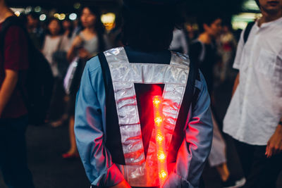 Rear view of man with illuminated stick standing in city