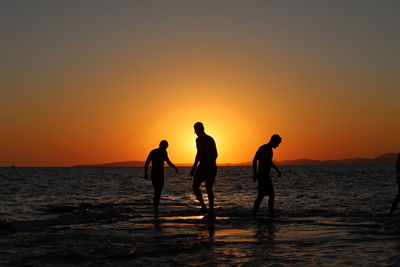 Silhouette people on beach against sky during sunset