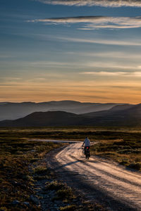 Female cyclist on the road from høvringen to smuksjøseter fjellstue, blåhøe 1617 meter in horisont