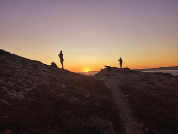 Silhouette people standing on beach against sky during sunset