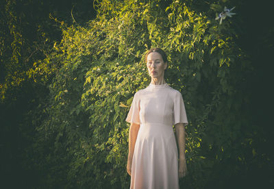 Woman in short pink dress in front of a hedge v