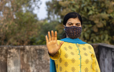 Indian woman showing open palm or stop gesture and looking at camera with nose mask on