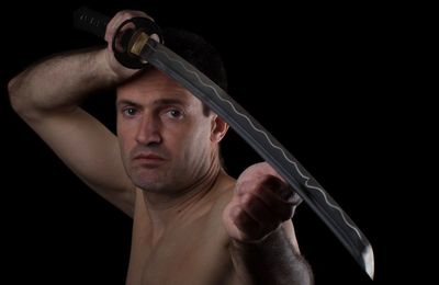 Close-up portrait of shirtless man holding sword over black background