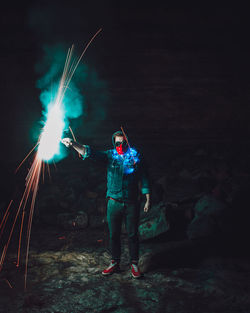 Man with firework standing on rock at night