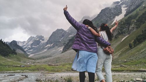 Rear view of friends standing on mountain against sky