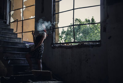 Young woman smoking while standing on steps in abandoned building