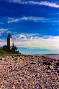 Lighthouse on beach by sea against sky