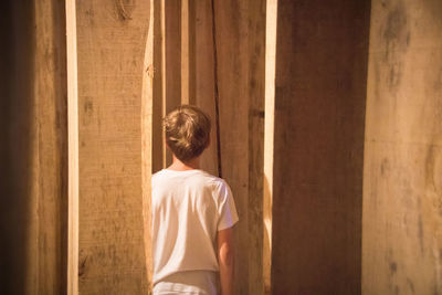 Rear view of boy standing amidst wooden planks