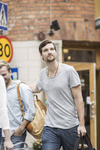 Thoughtful man carrying bag while walking with friends outdoors