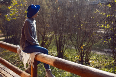 Village woman in a blue hat sits rear at a wooden house in autumn